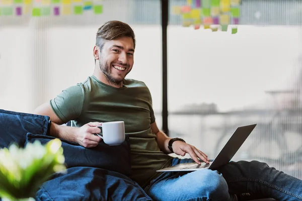 Mutlu genç adam rahat bir atmosferde dizüstü bilgisayar kullanarak