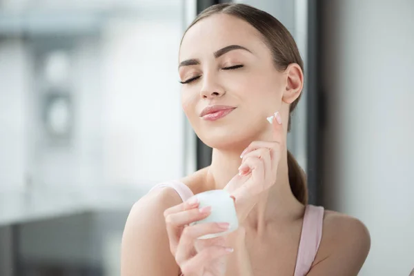 Chica alegre joven disfrutando mientras usa cosméticos faciales — Foto de Stock