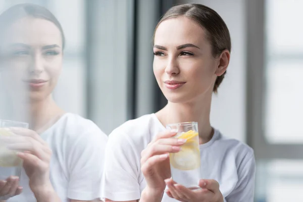 Feliz chica atractiva beber agua con limón fresco en el interior —  Fotos de Stock