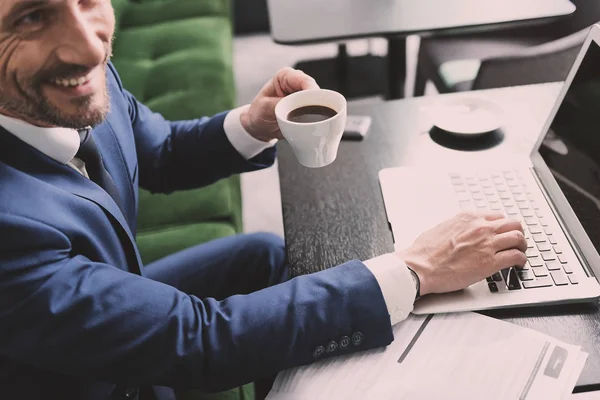 Gioioso uomo d'affari che gode di bevande calde durante il lavoro online — Foto Stock