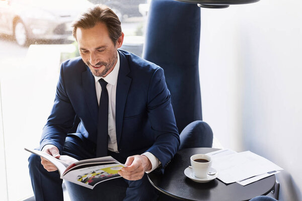 Joyful man in suit entertaining with journal in cafe