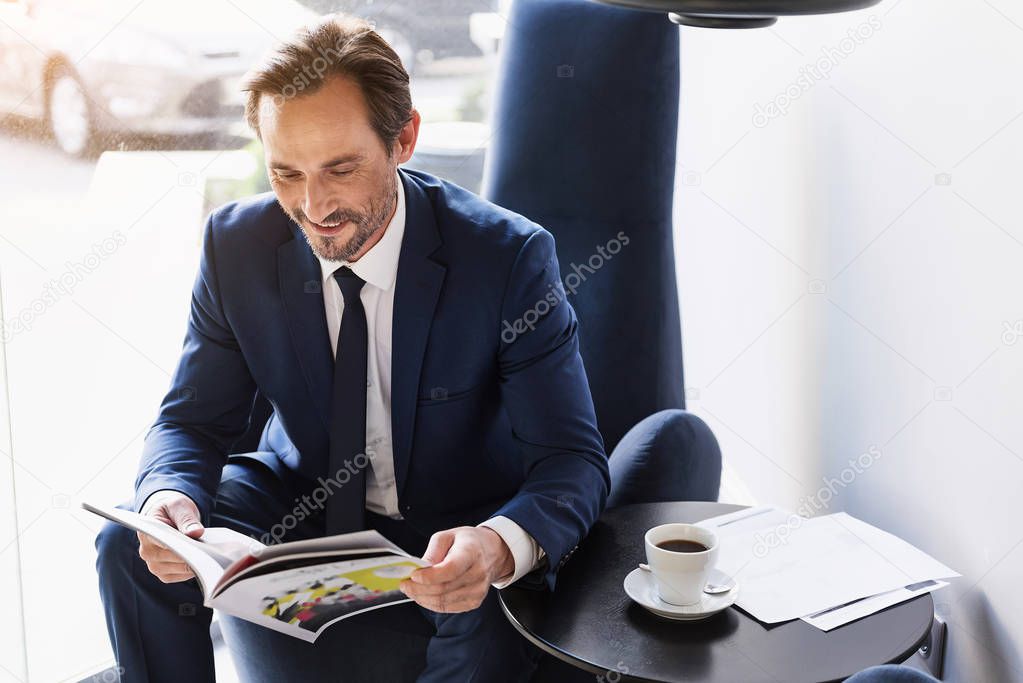 Joyful man in suit entertaining with journal in cafe