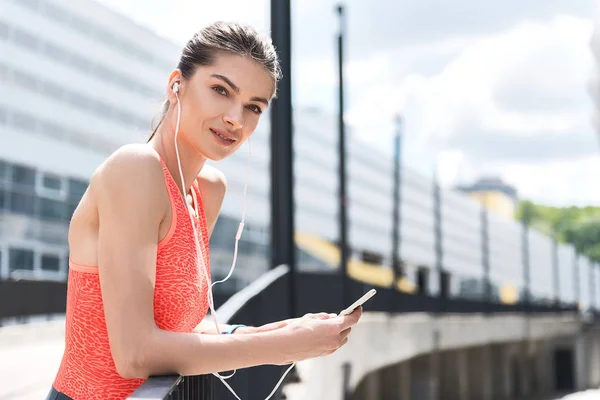 Chica deportiva alegre usando reproductor de teléfonos inteligentes después de hacer ejercicio —  Fotos de Stock