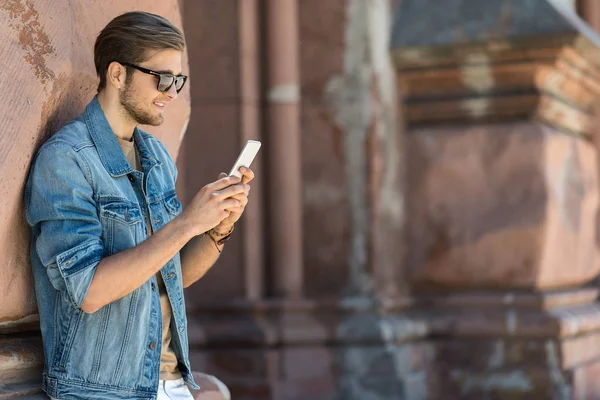 Glad ungdomlig skäggiga killen textning via gadget utomhus — Stockfoto