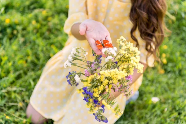 Csinos női gyermek gazdaság kis lepke közelében virágok — Stock Fotó