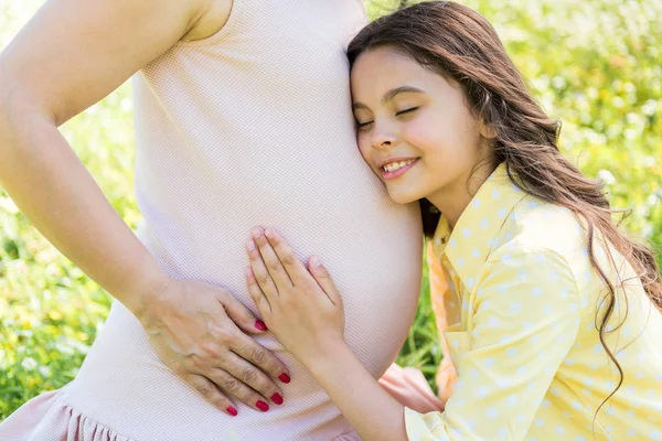 Aranyos lány próbál hallani a baba a mama hasában — Stock Fotó