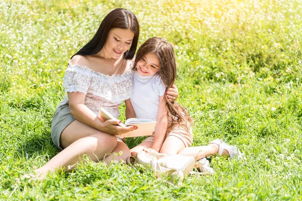 Donna gioiosa insegnare ragazza a leggere sul prato — Foto Stock