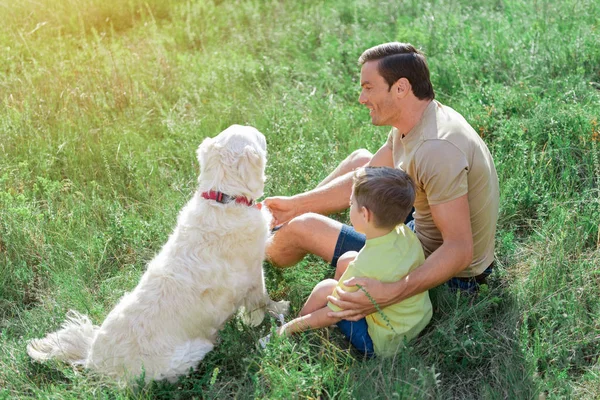 Cheerful father and kid having fun with puppy in nature
