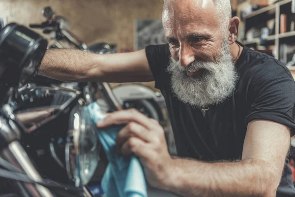 Happy smiling old man cleaning motorbike — Stock Photo, Image