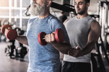 Sakallı ihtiyar profesyonel eğitmen ile spor salonunda egzersiz sahip