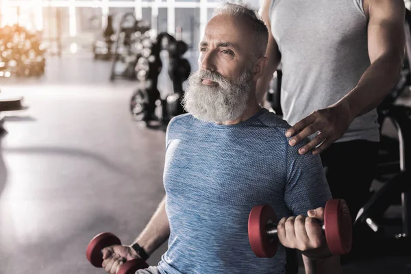 Серйозний бородатий пенсіонер проводить вправи в спортивному центрі — стокове фото