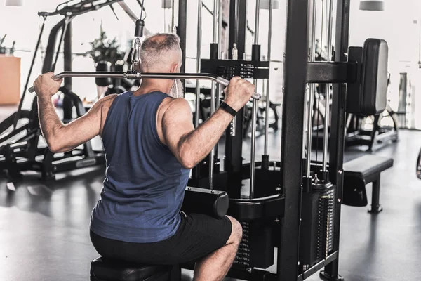 Concentrated senior male is doing exercises in modern gym — Stock Photo, Image