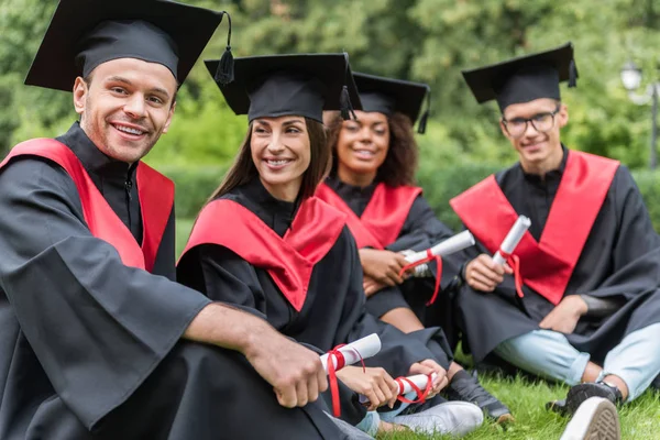 Cheerful graduates relaxing on green grass in campus