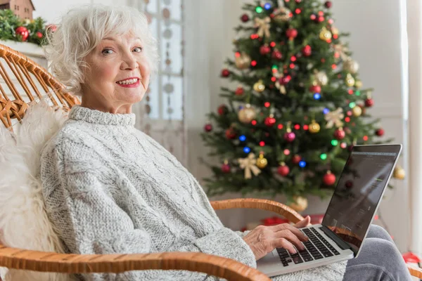 Щаслива старша жінка друкує на ноутбуці у свята — стокове фото