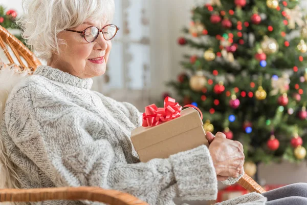 Okouzlující starší žena odpočívá doma s vánoční dárek — Stock fotografie