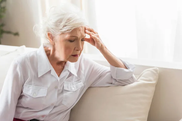 Äldre kvinna sitter på soffan och känner smärta — Stockfoto