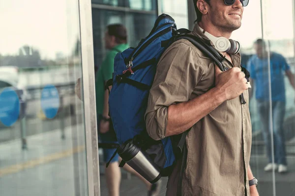 Positivo cara agradável com fones de ouvido está saindo do edifício do aeroporto — Fotografia de Stock