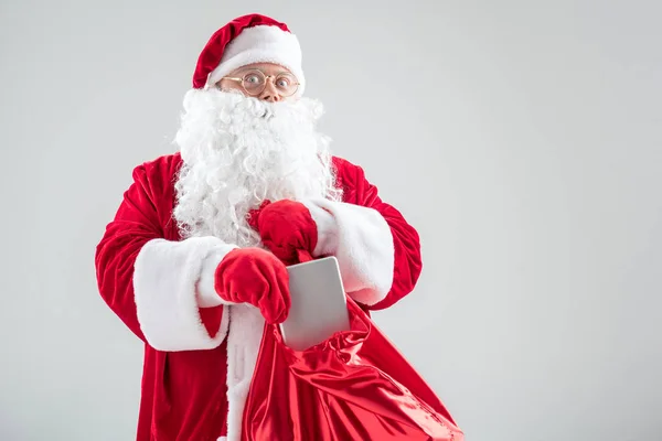 Podekscytowany Santa Claus ukrywanie tablet w czerwony worek — Zdjęcie stockowe