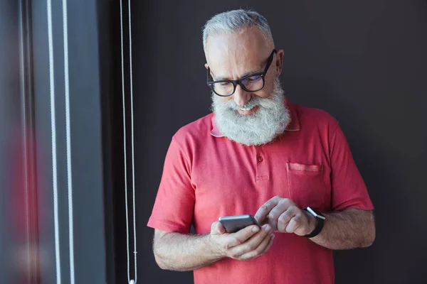 Cheerful old bearded man is holding smartphone with smile — Stock Photo, Image