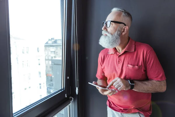 Serious viejo hombre de negocios de pelo gris está sosteniendo gadget moderno — Foto de Stock