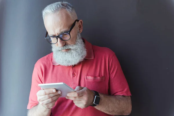 Pleasant senior man in glasses is using modern device — Stock Photo, Image