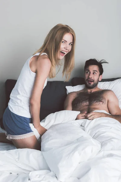 Vidám fiatal pár szórakozik a ágynemű — Stock Fotó