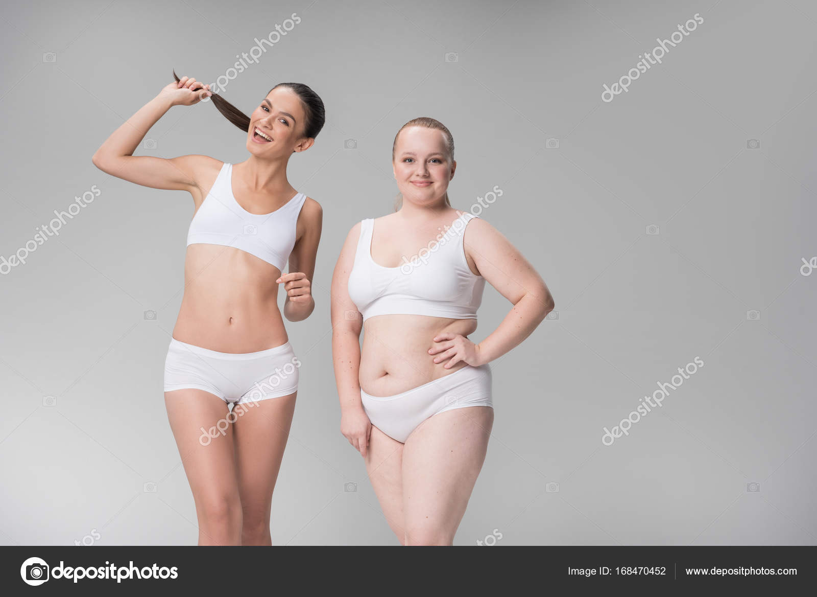 Portrait of two smiling women in great shape wearing tight underwear. They  are hugging and looking at camera with joy. Copy space in right side.  Isolated on background Photos
