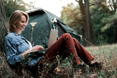 Neşeli kız ormanda taşınabilir bilgisayar kullanarak