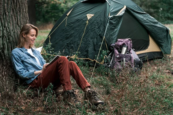 Alegre turista femenina relajándose en el bosque cerca de tienda — Foto de Stock