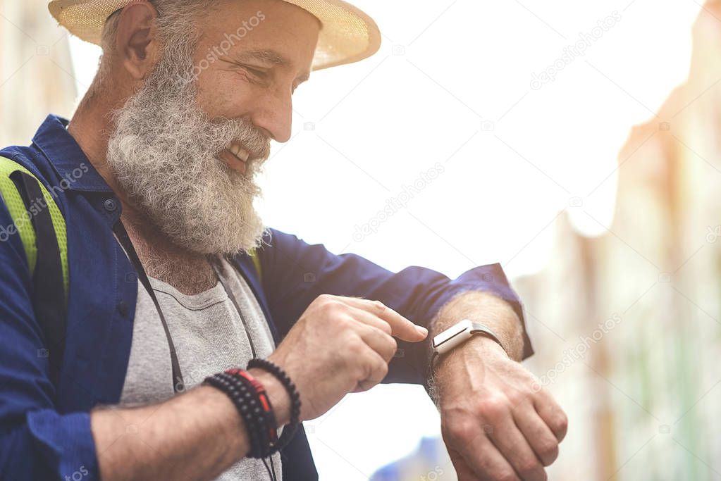 Joyful senior male tourist using smartwatch in town