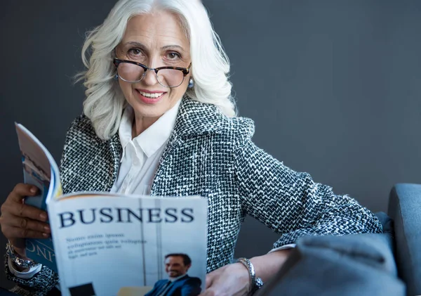 Positivo elegante velha mulher está desfrutando periódico no escritório — Fotografia de Stock
