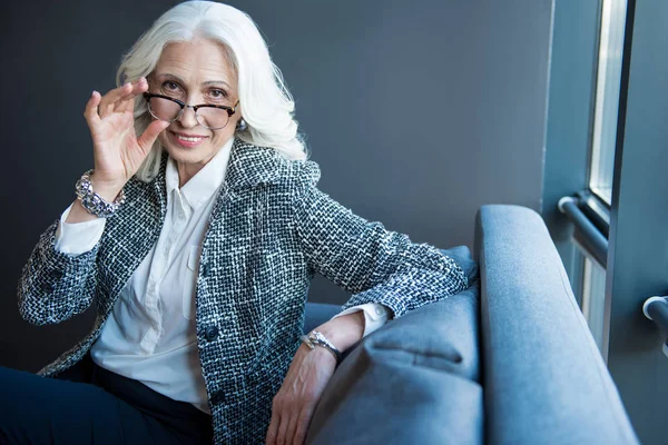 Positive senior elegant businesswoman is sitting on sofa — Stock Photo, Image