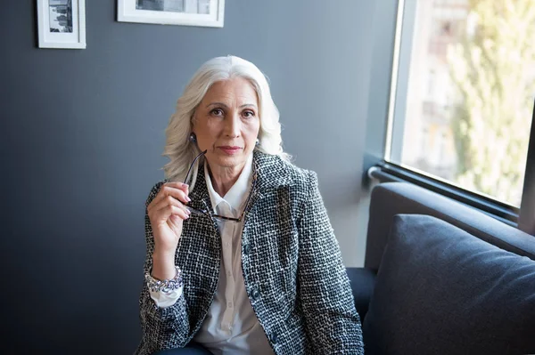 Pensiva signora anziana dai capelli grigi sta riposando sul divano — Foto Stock