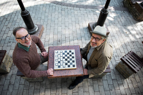 Joyful mature male pensioners entertaining with draughts