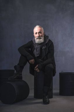 Ciddi tıraşsız emekli siyah varil üzerinde oturan