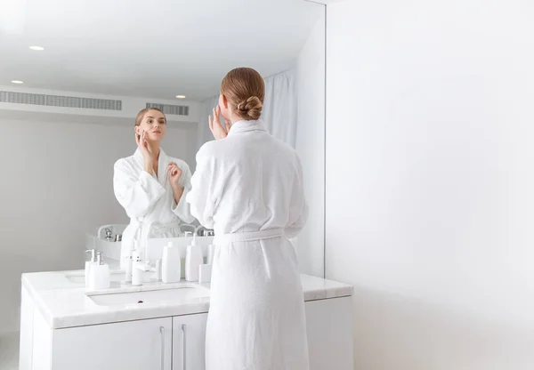 Привлекательная молодая женщина смотрит на свое отражение в ванной комнате — стоковое фото