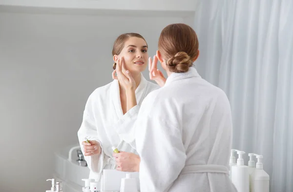 Menina bonita colocando creme em seu rosto no banheiro — Fotografia de Stock