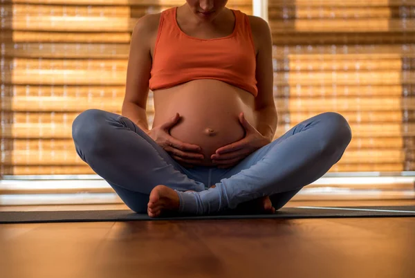 Mujer embarazada sentada en alfombra de yoga — Foto de Stock