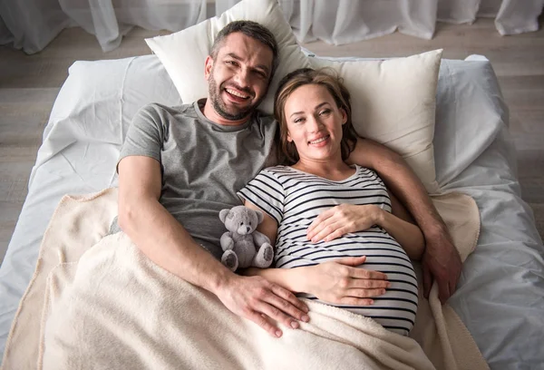 Vrolijke man omhelst zwangere vrouw op bed — Stockfoto