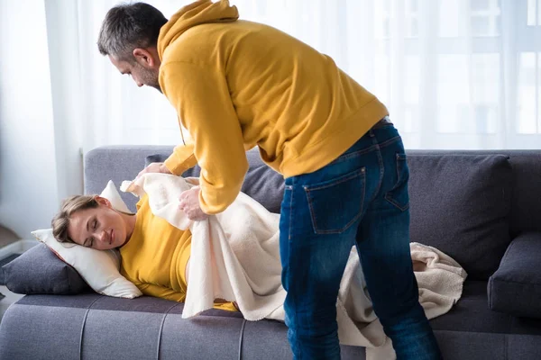 Hati-hati pria menempatkan selimut pada wanita yang diharapkan tidur siang di sofa — Stok Foto