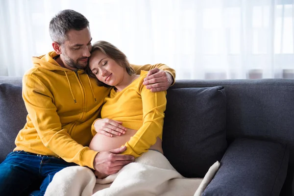 Щаслива вагітна подружня пара обіймає диван — стокове фото