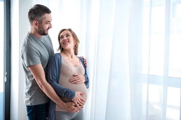 Радостная беременная женщина наслаждается объятиями мужа — стоковое фото
