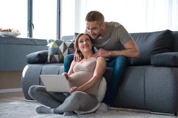 Vrolijke aanstaande moeder weergegeven: laptop aan haar echtgenoot — Stockfoto
