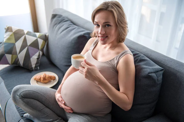 Fröhliche werdende Mutter frühstückt im Wohnzimmer — Stockfoto