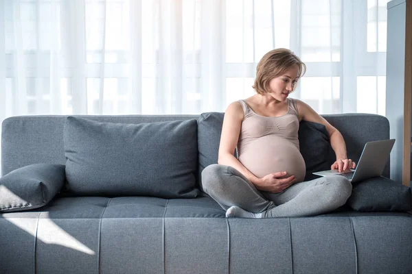 Vrolijke aanstaande moeder onderhoudend met zakboekje computer — Stockfoto