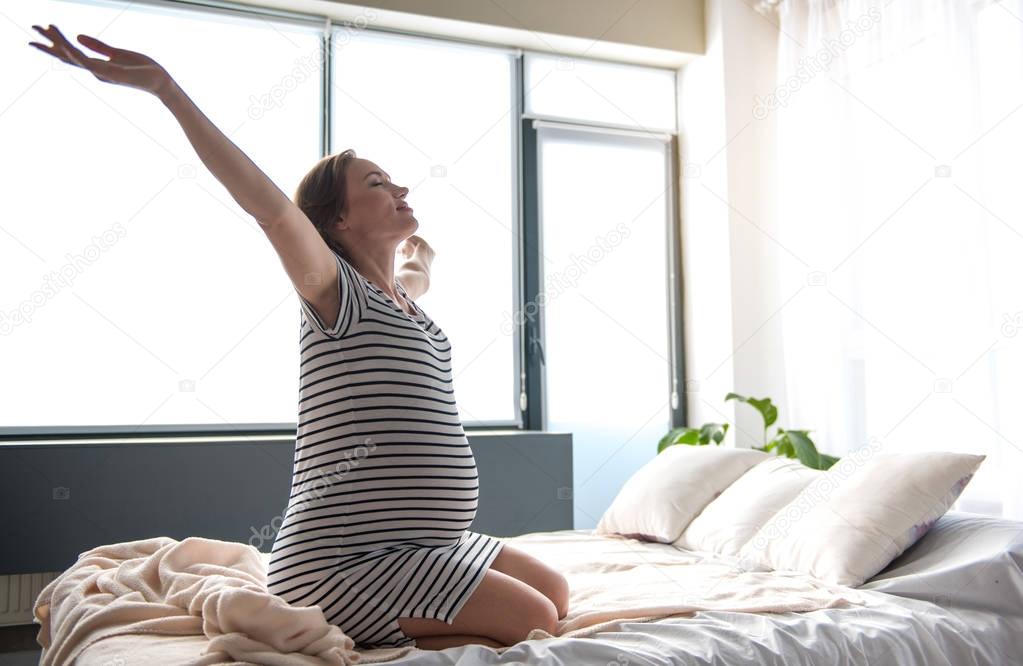 Excited expectant mother waking up in bedroom