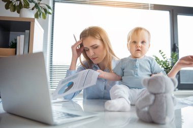 Weary mother working with baby in office clipart