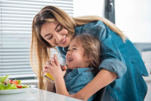 Affectionate asian woman hugging her child in kitchen — Stock Photo, Image