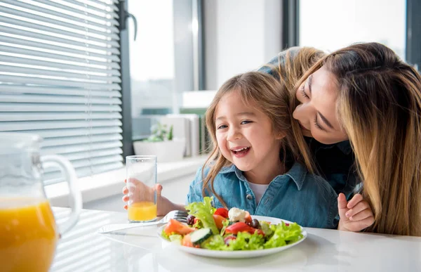 Pretty kid enjoying kiss of her mom during meal — Stock Photo, Image