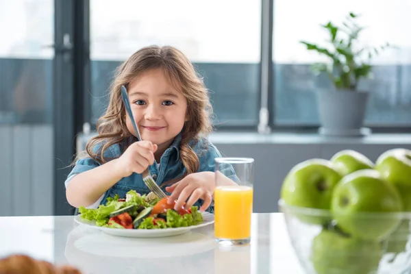 Cheerful asian girl eating salad in kitchen — Stock Photo, Image